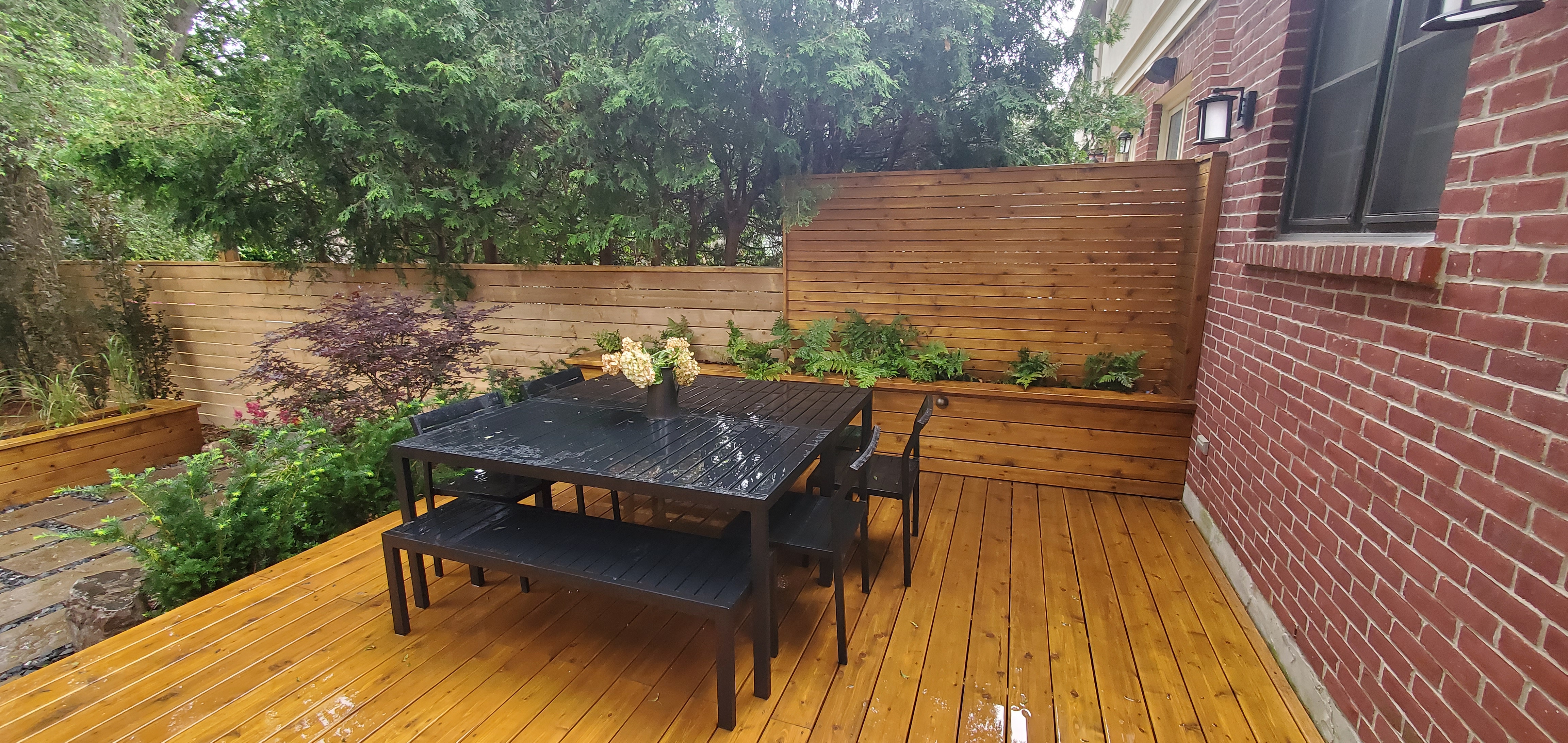 Retaining wall containing ferns alongside of outdoor dining table that seats eight
