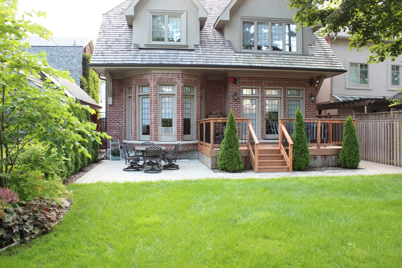 Backyard lawn space leading up to stone patio with decking