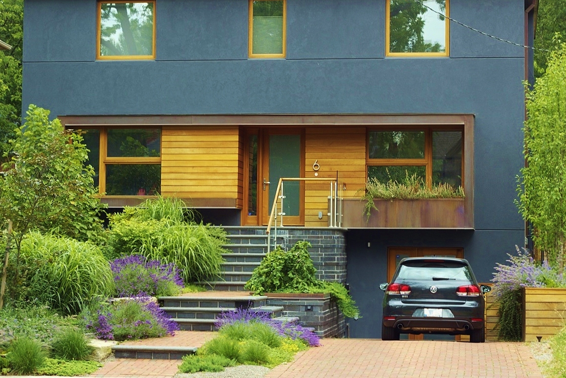 Front yard gardens with car parked. Stone interlock walkway to the front door matches rustic garden look